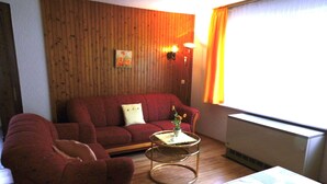 Ein Wohnzimmer mit einem roten Sofa, einem kleinen runden Tisch mit einer Vase und einer Heizung.