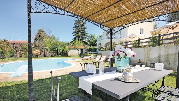 Eine Terrasse im Freien mit einem Essbereich, einem Pool im Hintergrund und einer überdachten Sitzgelegenheit.