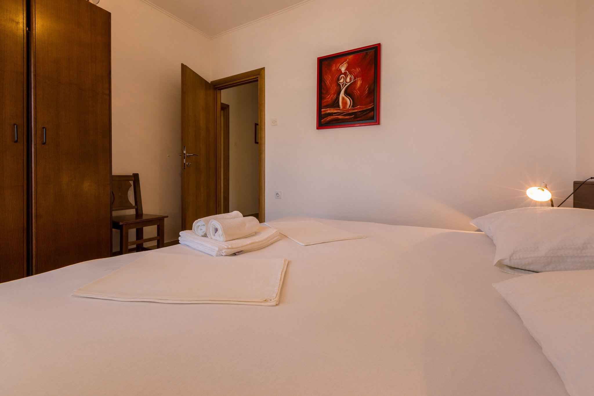 Een hotelkamer met een bed, een stoel, een houten garderobe en een schilderij aan de muur.