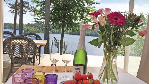 Une table dressée avec une bouteille de vin Cinzano, un saladier de fraises et un vase rempli de fleurs, donnant sur un lac.