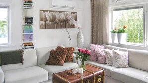 Un salon avec un canapé, une pile de livres, un vase de fleurs, un vase décoratif et une fenêtre ornée de plantes.