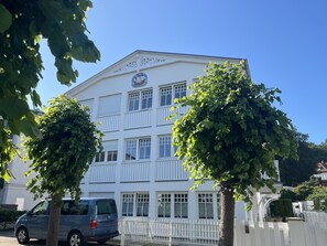 A multi-story building with a white facade, a balcony on the second floor, and a vehicle parked in front. - Villa Hansa, App. 4, 2 bedrooms, 2 bathrooms, in Binz, 2 balconies - App. with 2 bedrooms and 2 bathrooms (Binz)