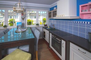A modern kitchen with a glass dining table, white cabinets, a blue and white tiled backsplash, and a view of the outside through large windows. - Villa Hansa, App. 4, 2 bedrooms, 2 bathrooms, in Binz, 2 balconies - App. with 2 bedrooms and 2 bathrooms (Binz)