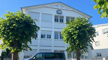 A multi-story building with a white facade, a ship logo, and a blue car parked in front.