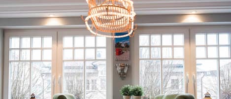 A dining area with a table, chairs, a hanging light fixture, and windows with a view.