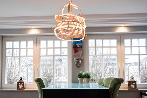 A dining area with a table, chairs, a hanging light fixture, and windows with a view.