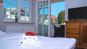 Et hotelværelse med en seng, et fjernsyn, en trækommode og en skydedør, der fører til en balkon.