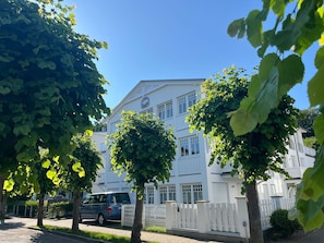 A multi-story building with a white facade, a visible logo, and a gated entrance. - Villa Hansa, App. 4, 2 bedrooms, 2 bathrooms, in Binz, 2 balconies - App. with 2 bedrooms and 2 bathrooms (Binz)