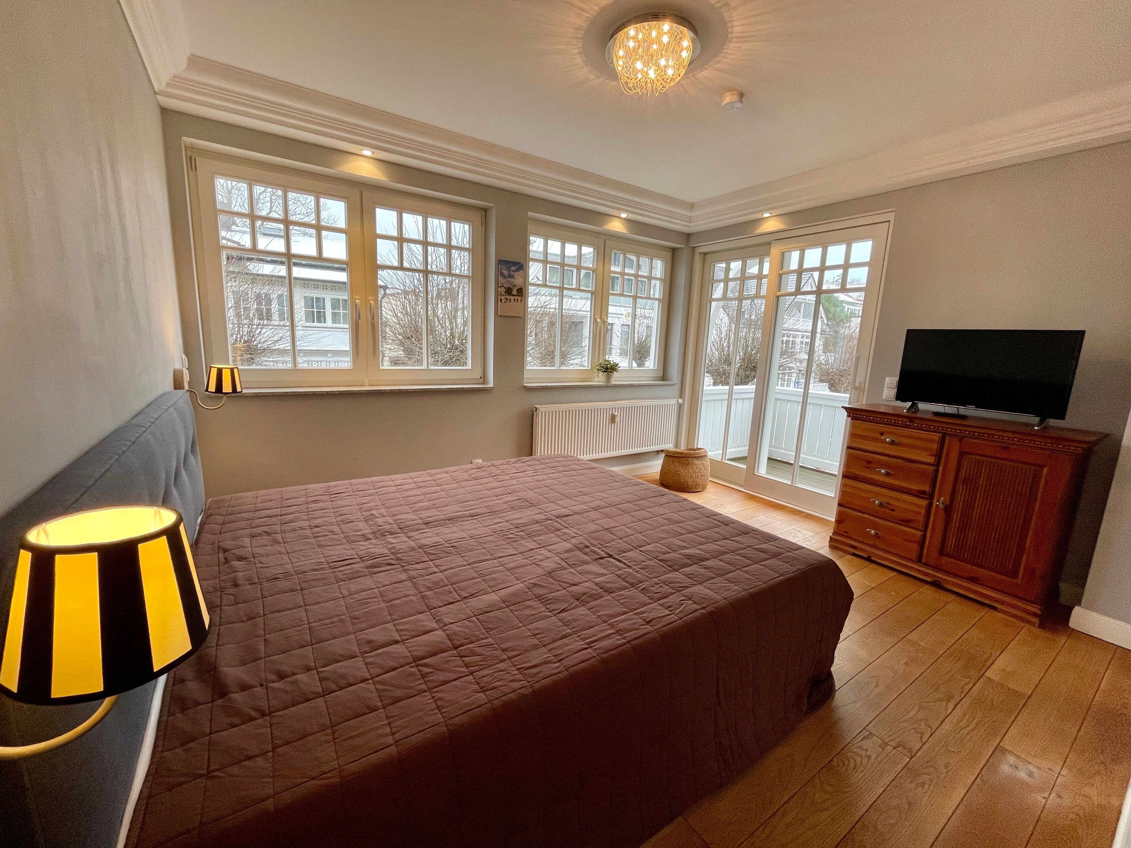 Ein Schlafzimmer mit einem großen Bett, einem Fernseher auf einer Holzkommode und einem Fenster mit Blick nach draußen.