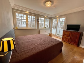 A bedroom with a large bed, a television on a wooden cabinet, and a window with a view of the outside. - Villa Hansa, App. 4, 2 bedrooms, 2 bathrooms, in Binz, 2 balconies - App. with 2 bedrooms and 2 bathrooms (Binz)