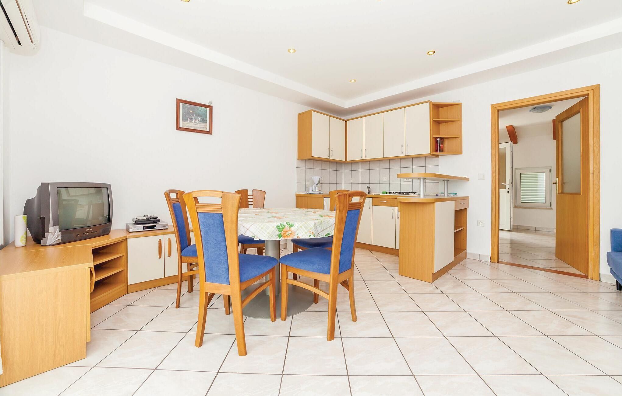 Una cocina compacta con comedor, que incluye una mesa con sillas, un televisor pequeño y un cuadro en la pared.
