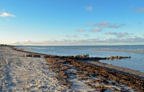 Une plage avec une digue rocheuse qui s’avance dans la mer, un rivage sablonneux et un ciel dégagé.