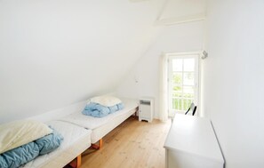 Une petite chambre lumineuse située sous les combles, avec deux lits simples, un bureau blanc et une fenêtre donnant sur un paysage verdoyant.
