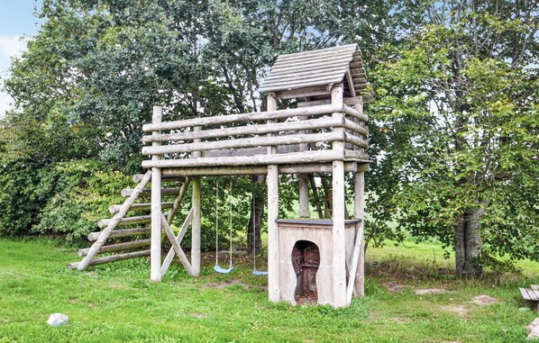 A wooden playhouse with a ladder, a swing, and an entrance.