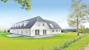 Une grande maison blanche avec un toit à forte pente, de nombreuses fenêtres et une pelouse bien entretenue.