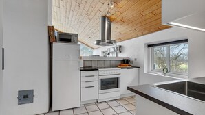 Moderni keittiö, jossa on valkoiset kaapit, ruostumattomasta teräksestä valmistettu liesi ja suuri ikkuna, josta avautuu näkymä puita kohti.