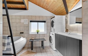 A compact kitchen with a washing machine, a sink, and a window with a plant.