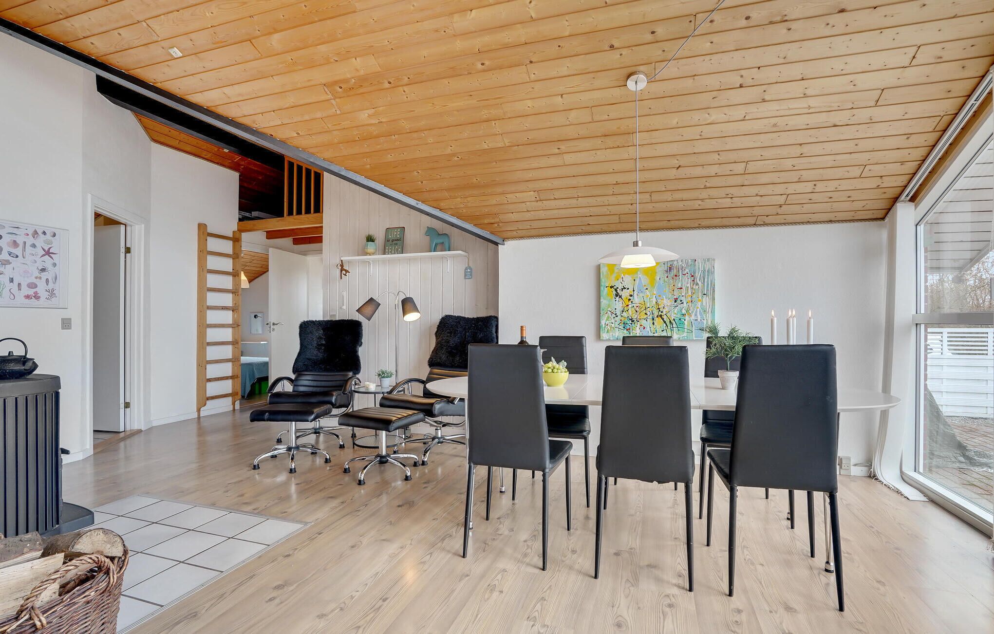 A modern dining area with a wooden ceiling, black chairs, a round table, and a large window.