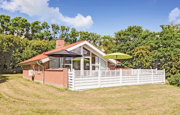 A single-story brick house with a red roof, a covered porch, and a white fence.