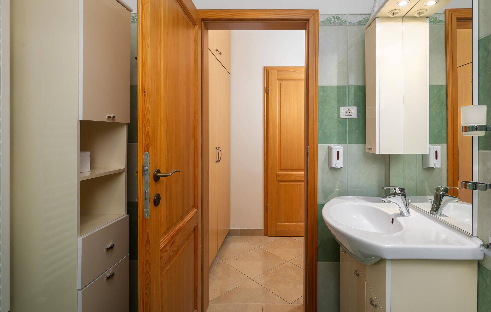 Een badkamer met twee wastafels, een spiegel en een houten deur naar een andere kamer.