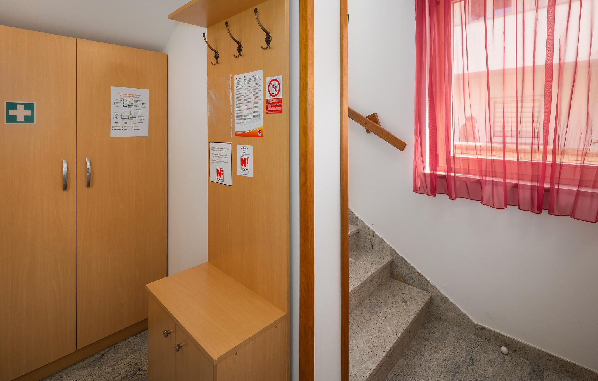 A wooden wardrobe with a bench, a staircase, and a window with sheer curtains.