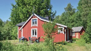 A red wooden cabin with two windows, a small porch, and a table with chairs.