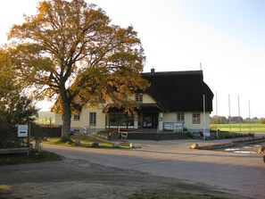Een traditioneel gebouw met rieten dak, een geplaveid pad en een bord dat een nabijgelegen loch aangeeft.
