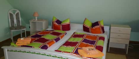 A bed with a colorful quilt, pillows, a nightstand, a chair, and a drawer unit.