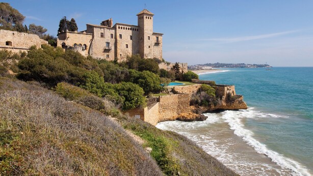 A coastal castle with a tower, surrounded by greenery and overlooking the sea.
