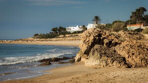 A beach with rocky cliffs, a sandy shore, and buildings in the background.