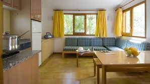 A compact kitchen with a dining area, a built-in bench, and a window with yellow curtains.