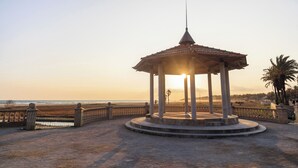 A gazebo with a tiled roof and a central pole, surrounded by a stone fence, overlooking a beach.