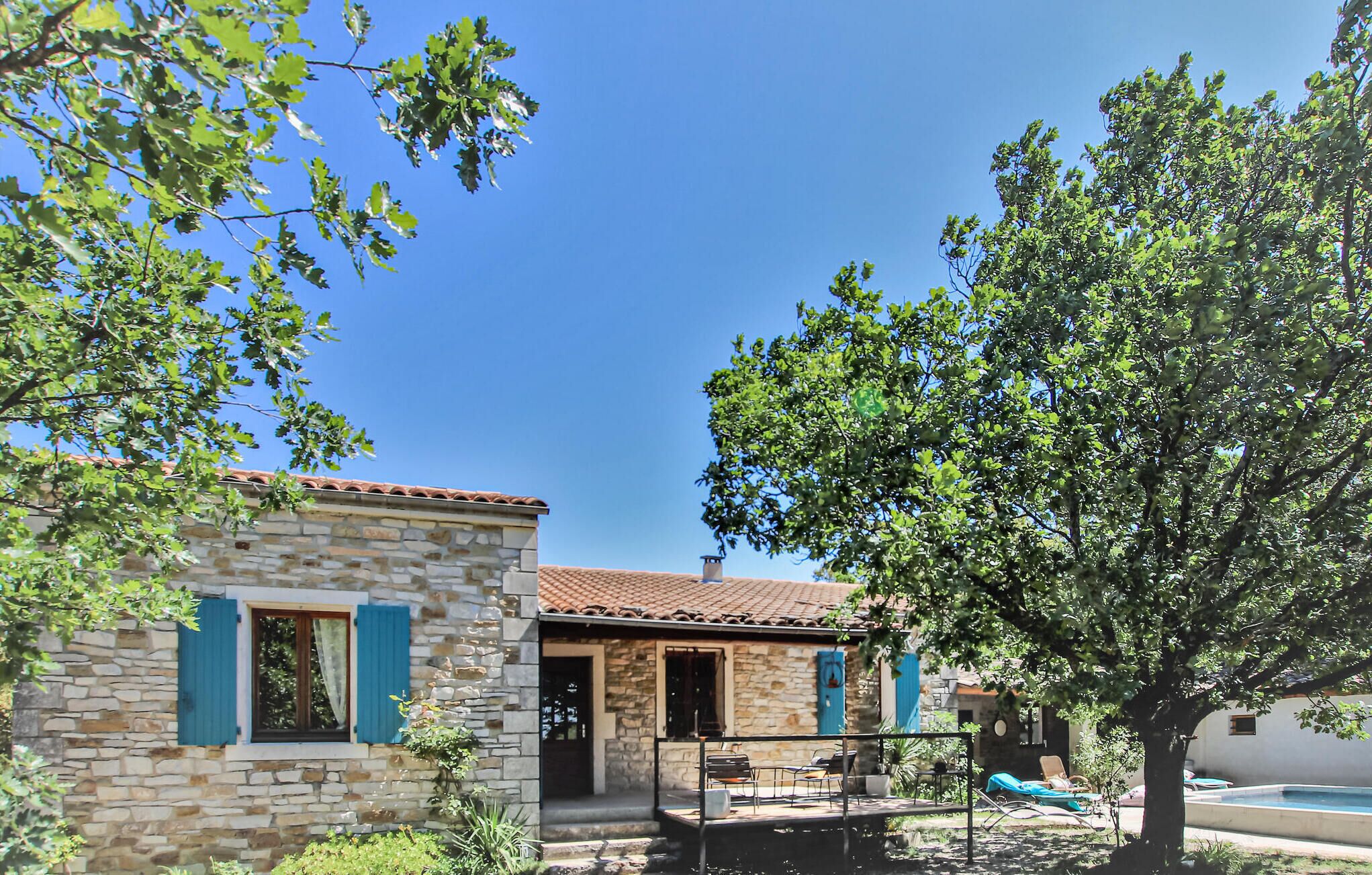 Une maison en pierre avec un toit en tuiles, un petit patio avec des meubles d’extérieur et une piscine.