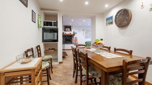 Zona pranzo con tavolo e sedie in legno, una ciotola di frutta e una cucina con forno a microonde e forno.