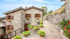 Una casa in pietra con persiane di legno, un piccolo portico e piante in vaso.