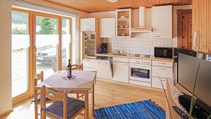 Kompakti keittiö, jossa on puiset kaapit, mikroaaltouuni, kahvinkeitin sekä ruokailutila, jossa on pöytä ja tuolit.