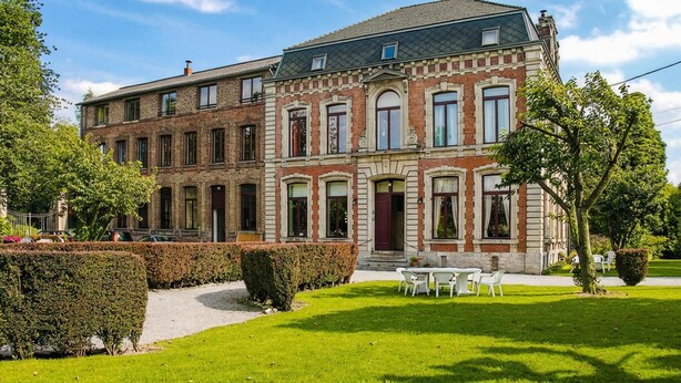 A large, multi-story building with a symmetrical facade, featuring a mix of brick and stone materials, and a central entrance with a red door. - Lovely home in Quiestède with sauna (Quiestède)
