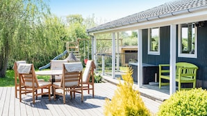 Eine Holzterrasse mit Tisch und Stühlen, einer Rutsche und einem überdachten Sitzbereich mit einer Bank.