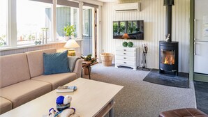 Ein gemütliches Wohnzimmer mit einer Couch, einem Tisch mit Strickzeug, einem Fernseher, einem Kamin und einem Fenster mit Jalousien.