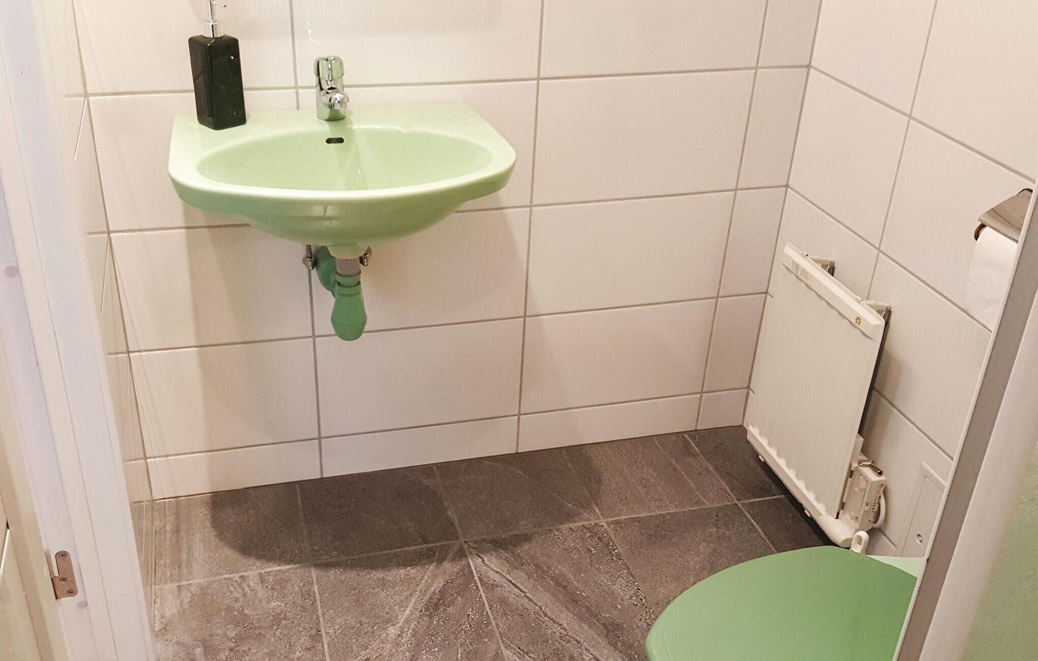 Une salle de bain avec un lavabo vert, des toilettes et un mur recouvert de carreaux blancs.