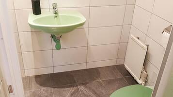 A bathroom with a green sink, a toilet, and a white tiled wall.