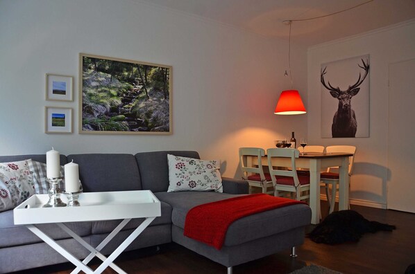 A living room with a sofa, a dining table, a red lamp, and a framed deer picture.