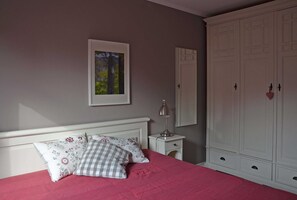 A bedroom with a bed, a nightstand, a lamp, a wardrobe, and a framed picture on the wall.