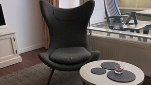 A modern living room with a grey armchair, a round coffee table, and a view of the outdoors through a window. - Vacation apartment Kleine Fluchten - Holiday apartment (Sankt Andreasberg)