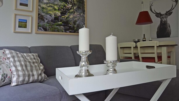 A living room with a grey sofa, a white coffee table with two candles, framed pictures on the wall, and a red pendant light. - Vacation apartment Kleine Fluchten - Holiday apartment (Sankt Andreasberg)