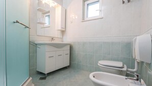 Ein Badezimmer mit Waschbecken, Toilette und Badewanne. Über der Toilette befindet sich ein Fenster und über dem Waschbecken ein Spiegel.
