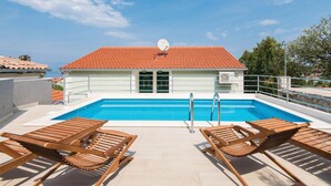 Ein Pool auf dem Dach mit einer Satellitenschüssel, umgeben von Holzliegen und einem Gebäude mit roten Ziegeln.