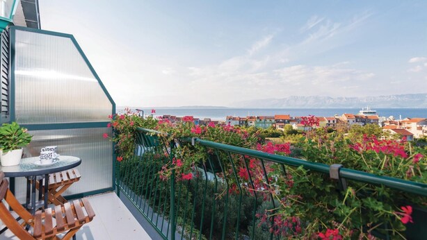 Ein Balkon mit Tisch und Stühlen, einem Blumentopf und Blick auf eine Küstenstadt mit Gebäuden und Bergen in der Ferne.