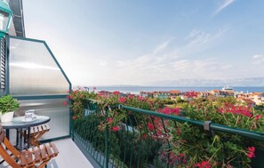 A balcony with a table and chairs, a potted plant, and a view of a coastal town with buildings and mountains in the distance. - 1 bedroom cozy apartment in Trpanj (Trpanj)