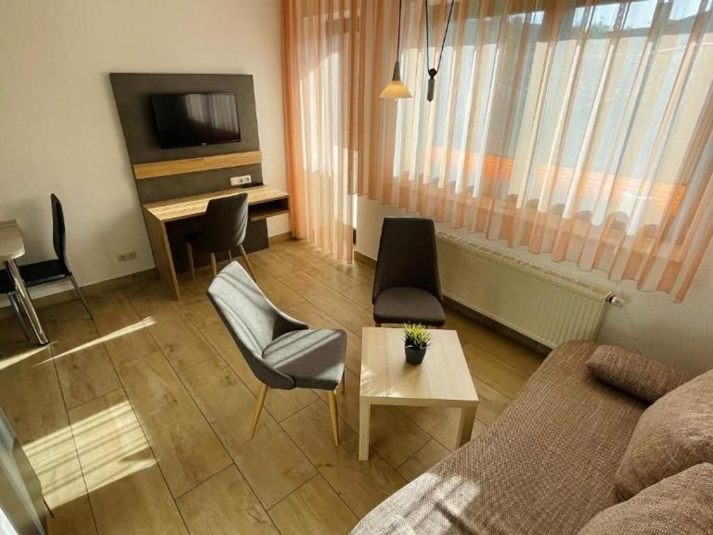 Ein modernes Wohnzimmer mit einer Couch, zwei Sesseln, einem Couchtisch, einem Fernseher und einem Essbereich.